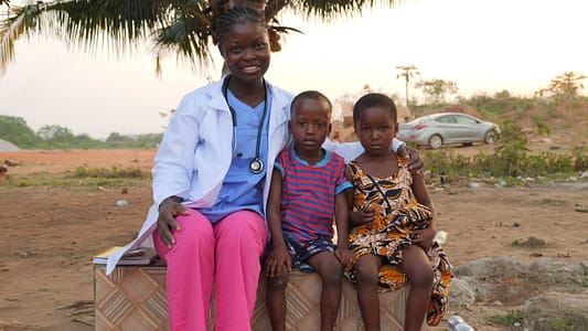 pexels photo 34717769 Female healthcare worker smiles with two children outside, showcasing community care.